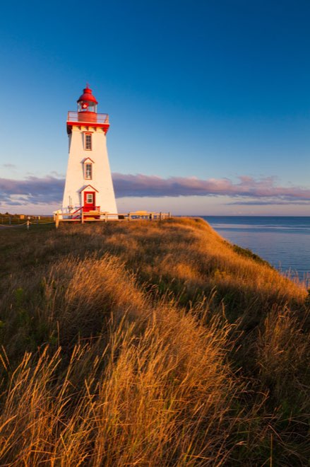 Souris East Lighthouse, red and white, standing above the grass at sunset